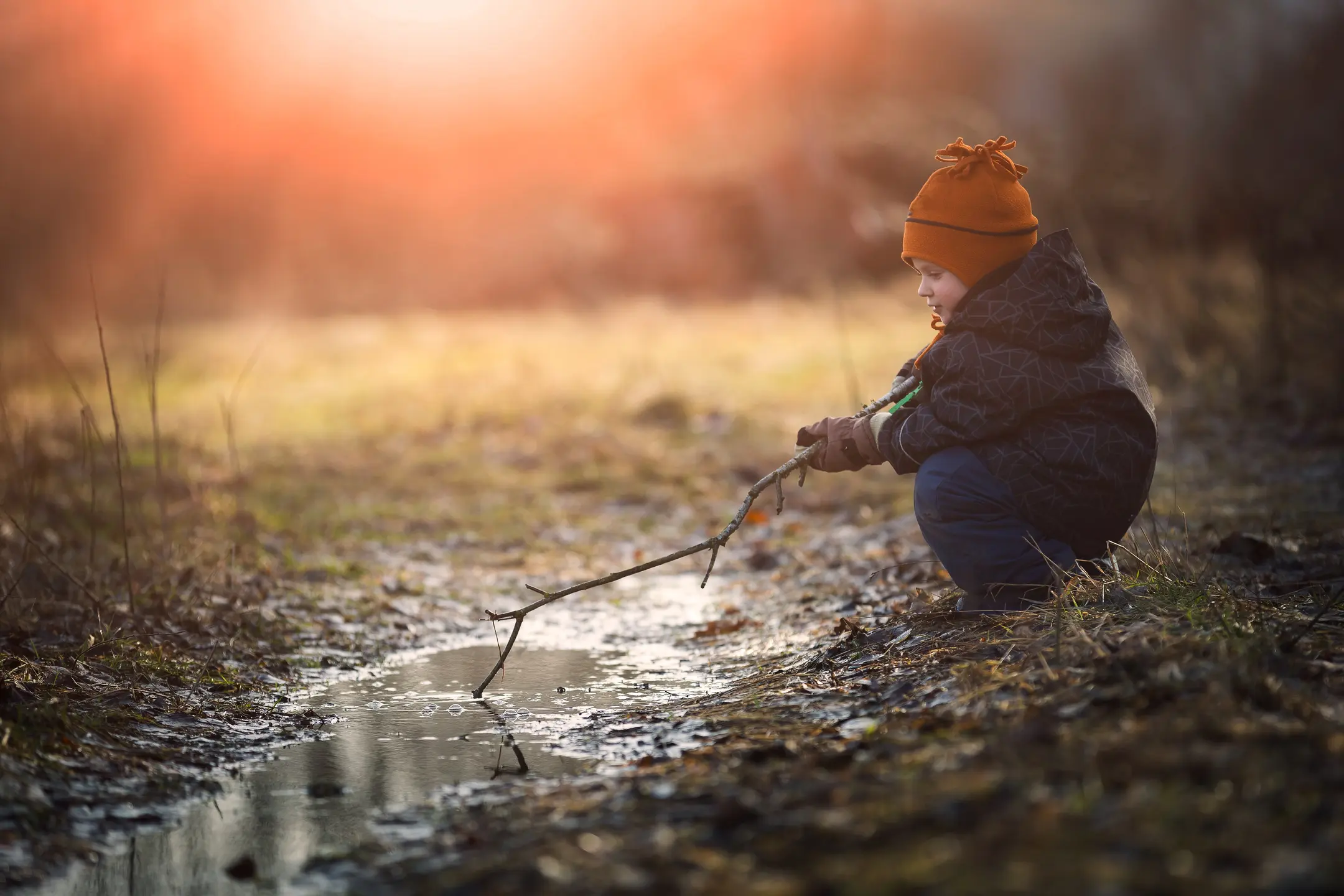 young child plays with stick outside in puddle