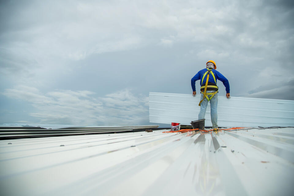 commercial roof maintenance-roofing worker in a safety harness installing new white metal roofing panel