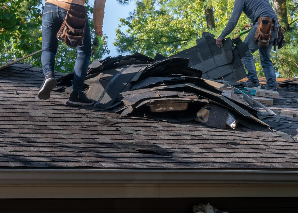 how to get insurance to pay for roof replacement-close up of two roofers removing old roofing materials