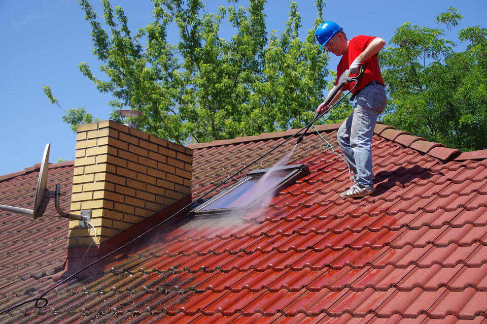 roof washing-man standing on red roof powerwashing the shingles