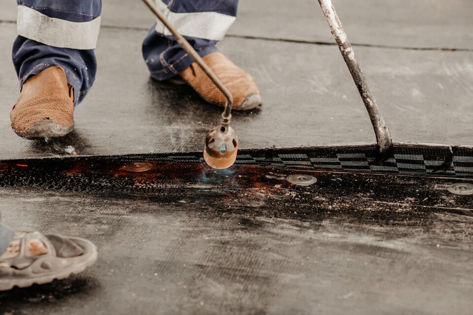 commercial roof leak repair-close up of roofer repairing section of commercial flat roof
